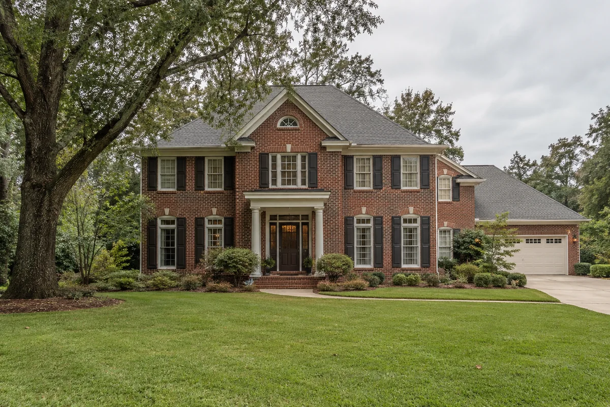 Red brick two-story home with white trim and mature trees.